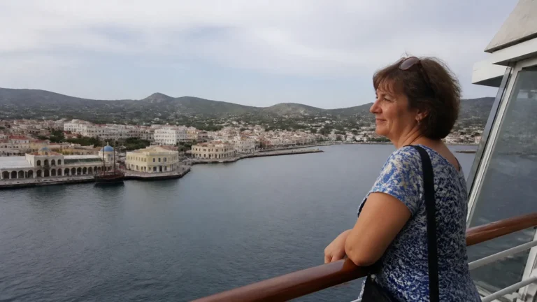 Passenger looks across a harbor town from a ship's railing.
