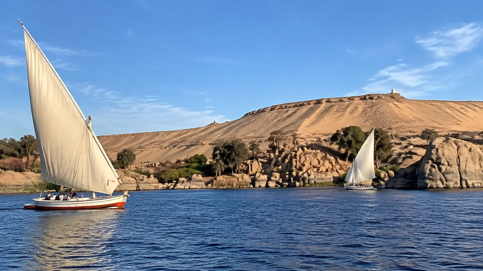 Feluccas sailing on the Nile beside rocky desert banks.