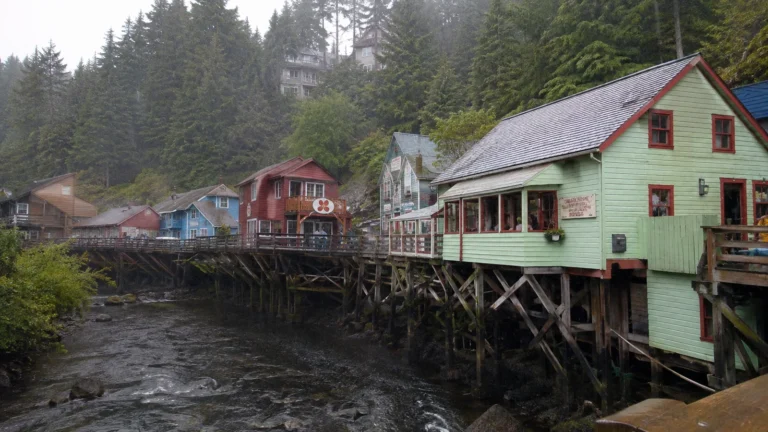 Colorful wooden stilt buildings beside a creek beneath evergreen trees.
