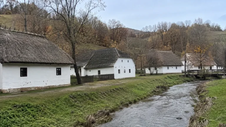 White traditional cottages beside a stream and grassy banks.