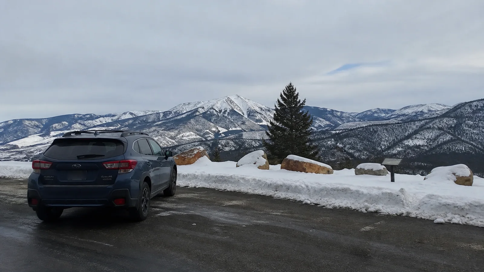 Car parked at a snowy overlook facing a rugged mountain range.