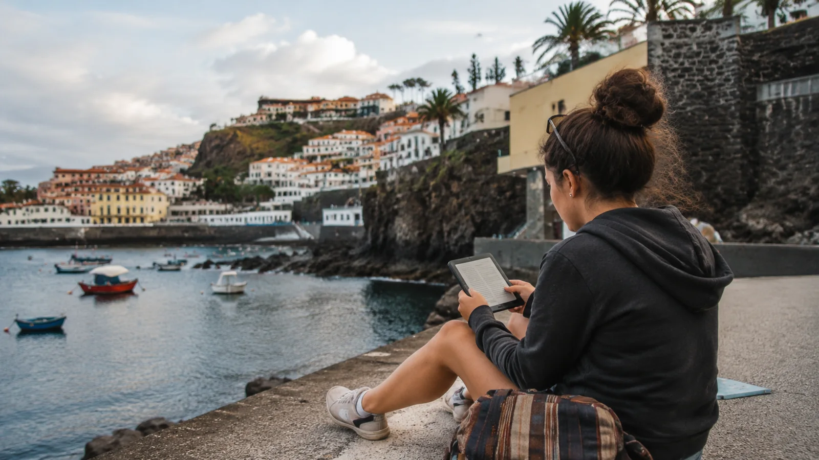 Woman sitting beside a harbor and reading an e-reader