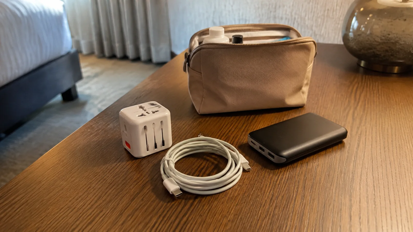 Travel adapter, charging cable, power bank, and tan pouch on a table.
