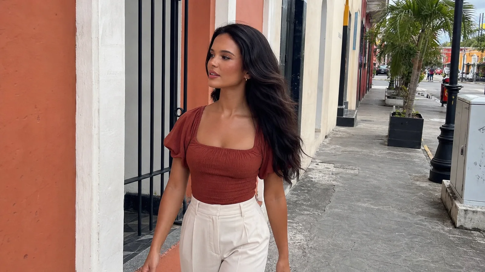 Woman walks beside colorful buildings along a palm-lined sidewalk.