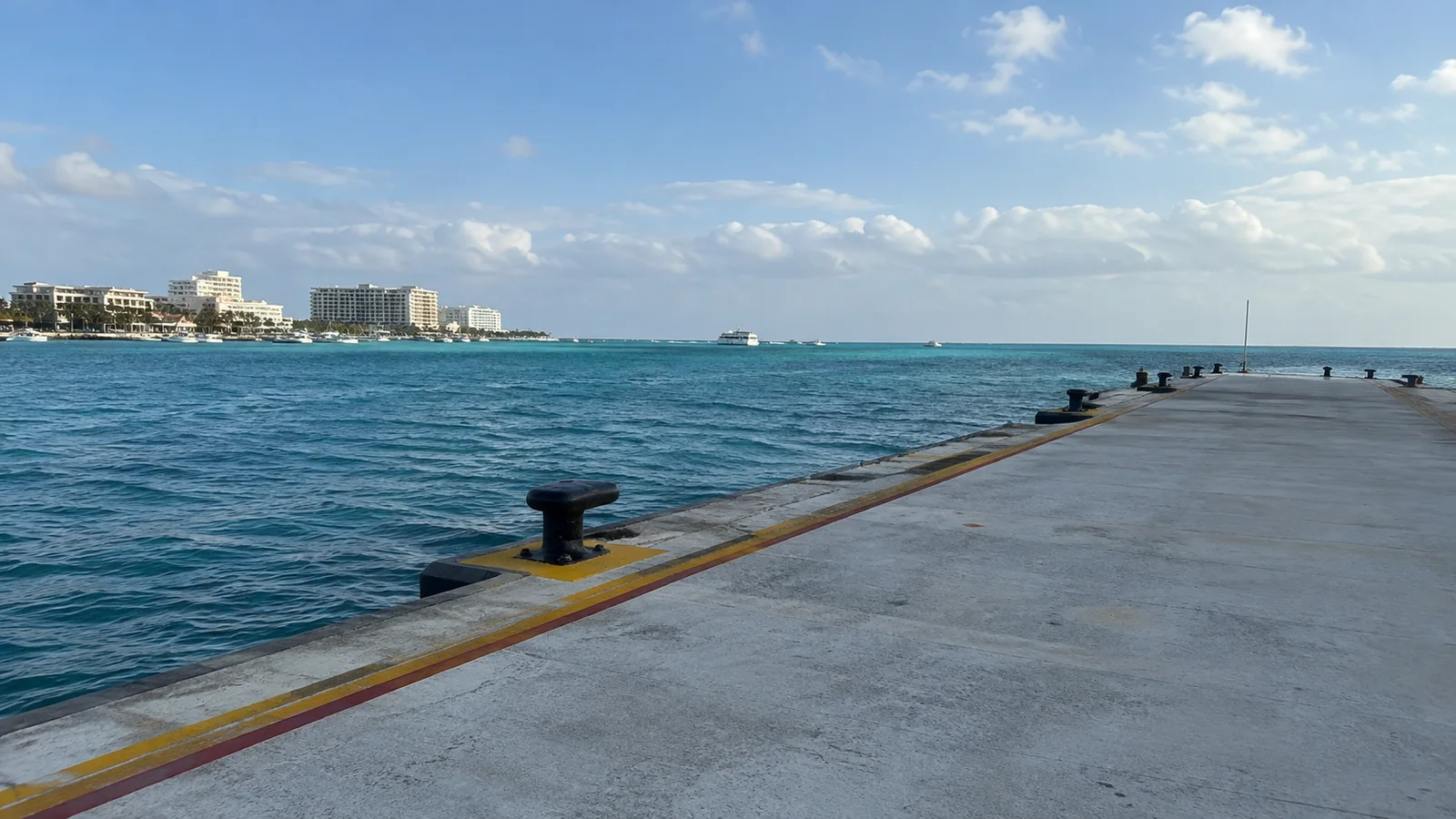 Concrete waterfront pier extends beside bright blue water.
