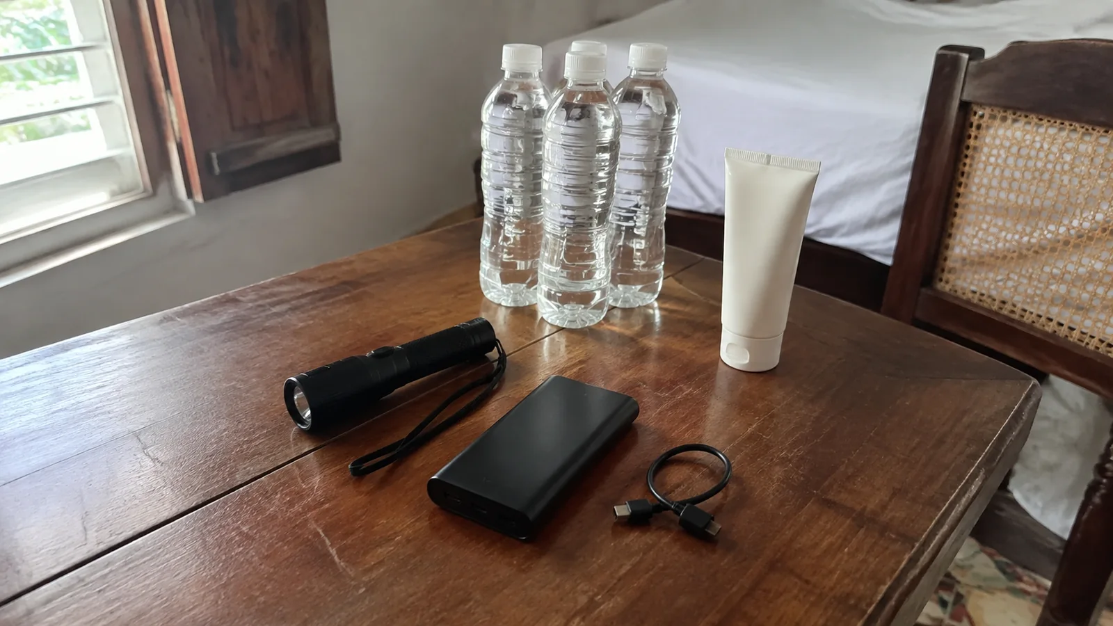 Water bottles, sunscreen, flashlight, and portable charger rest on a table.