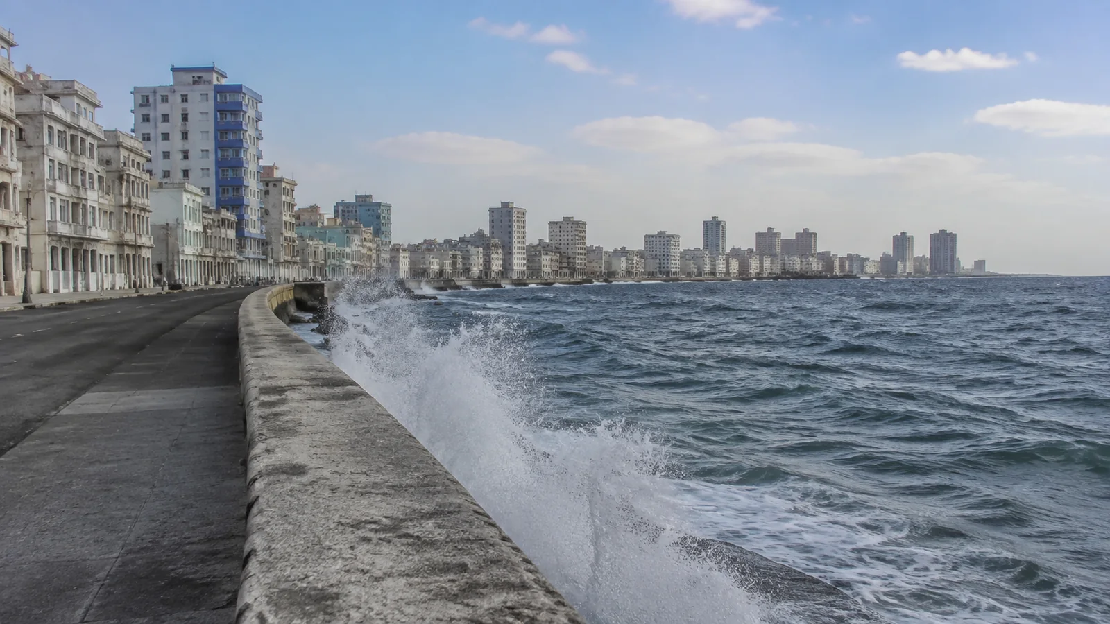 Waves break against a seawall beneath a long city waterfront.