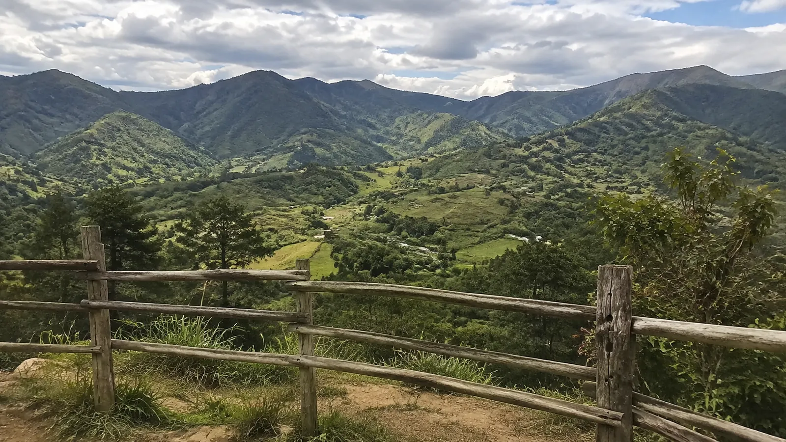 Wooden fence overlooks lush green mountains and cultivated valleys.