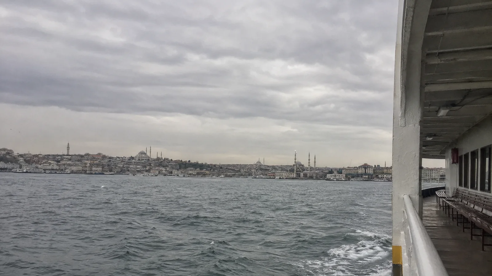 View from a ferry across the water toward a city skyline and minarets.