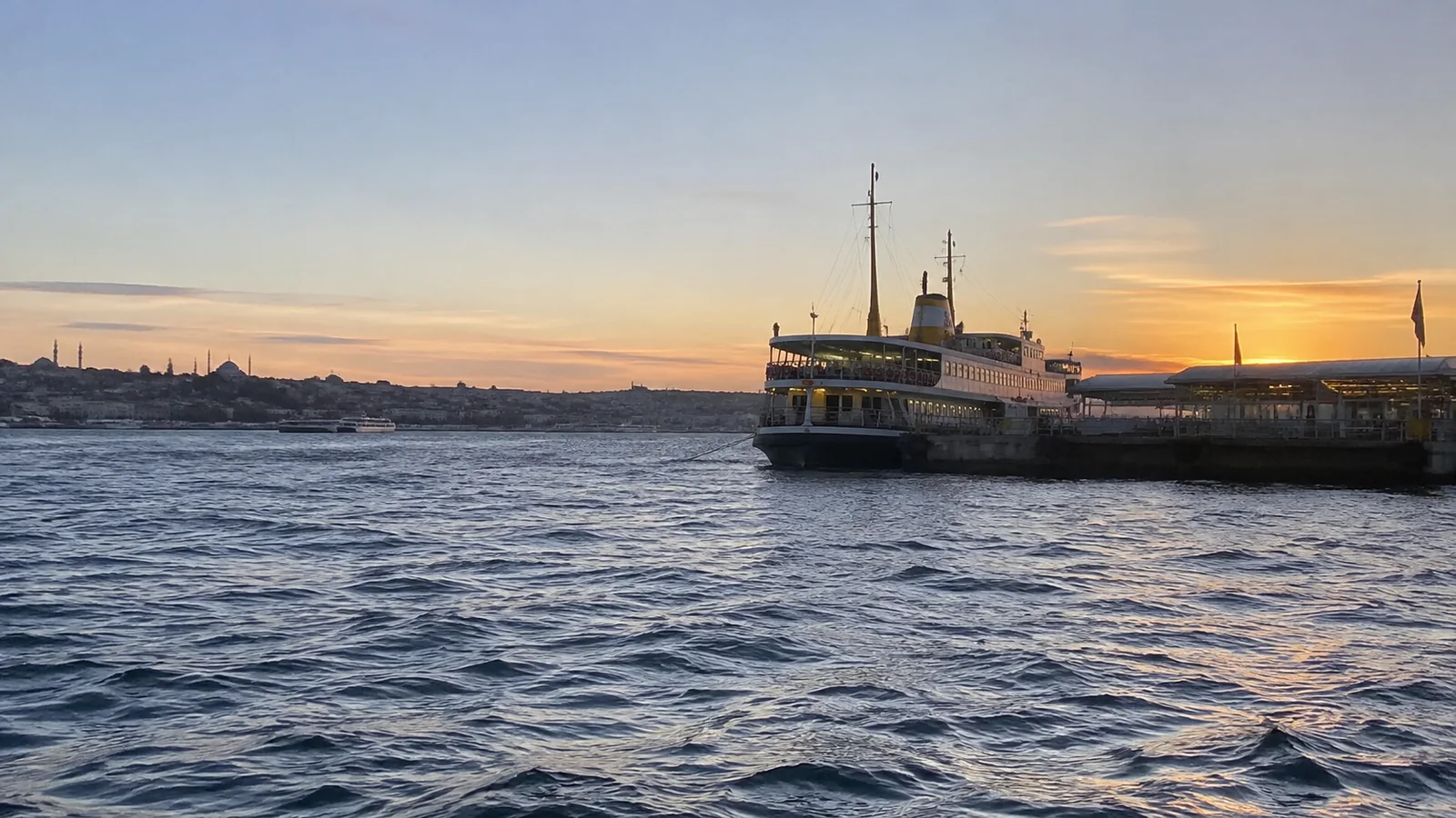 Ferry crosses the water beside a city skyline at sunset.