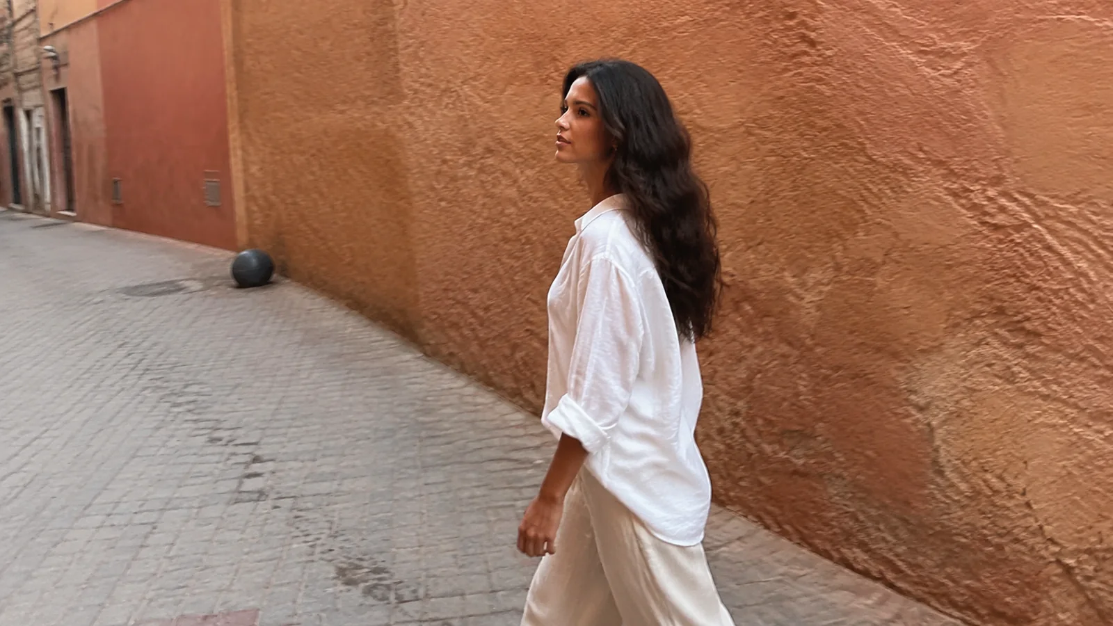 Woman walks beside a long terracotta-colored wall.