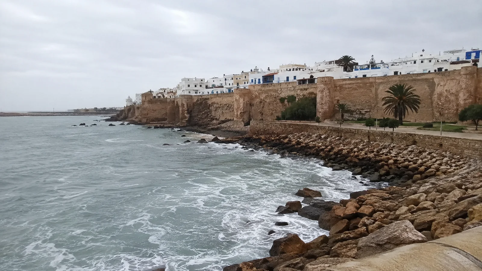 Fortified coastal walls rise above a rocky shoreline and breaking waves.