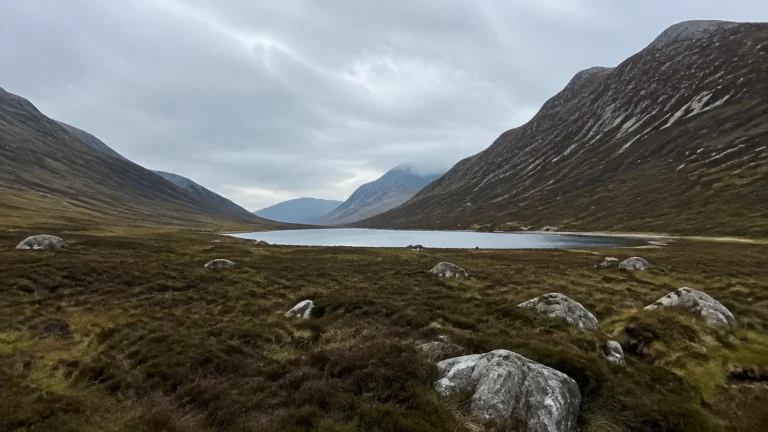 Narrow lake lies between steep grassy mountains beneath gray clouds.