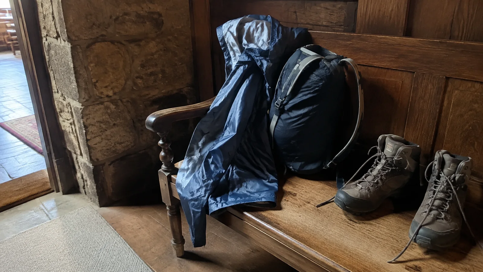 Rain jacket, backpack, and hiking boots rest on a wooden bench.