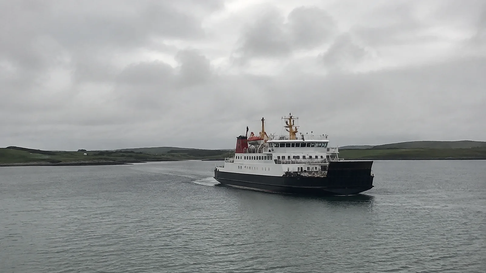 Ferry sails across gray water near low green islands.