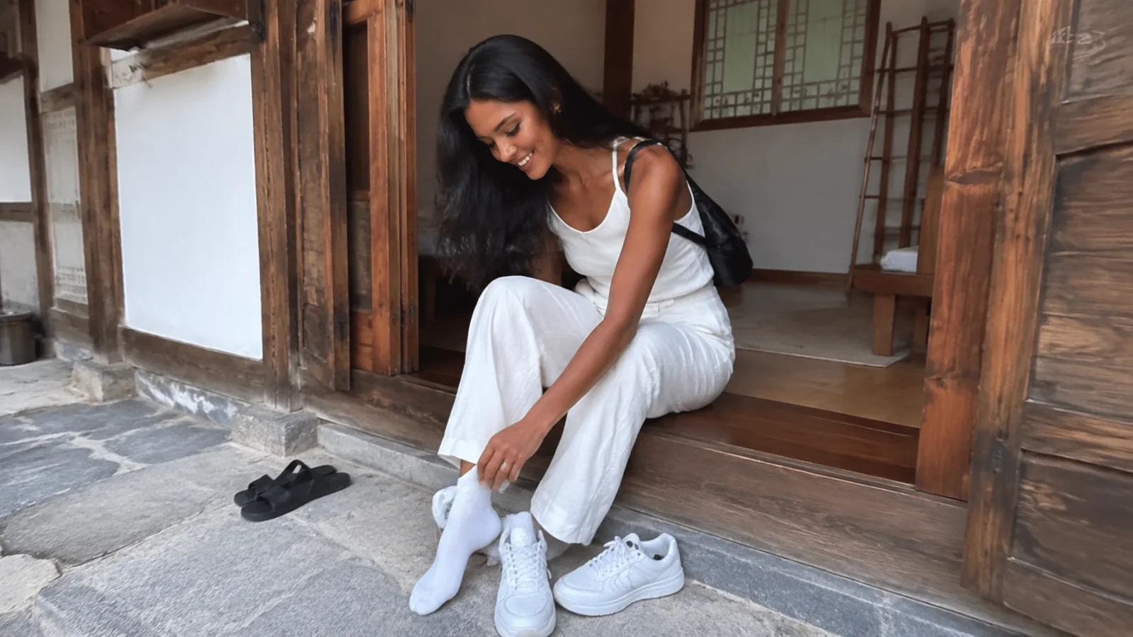 Woman adjusts her shoe while seated at a traditional wooden doorway.