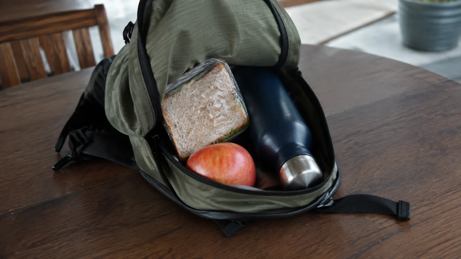 Sandwich, apple, and reusable bottle packed inside an open backpack.