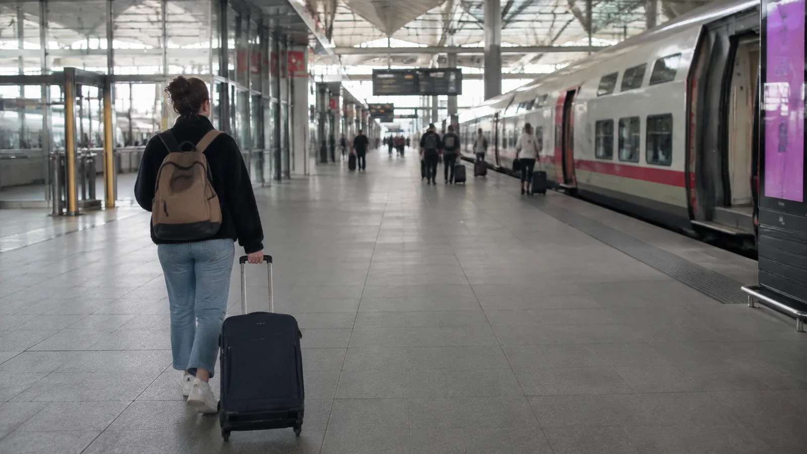 Traveler wheeling a suitcase along a railway platform.