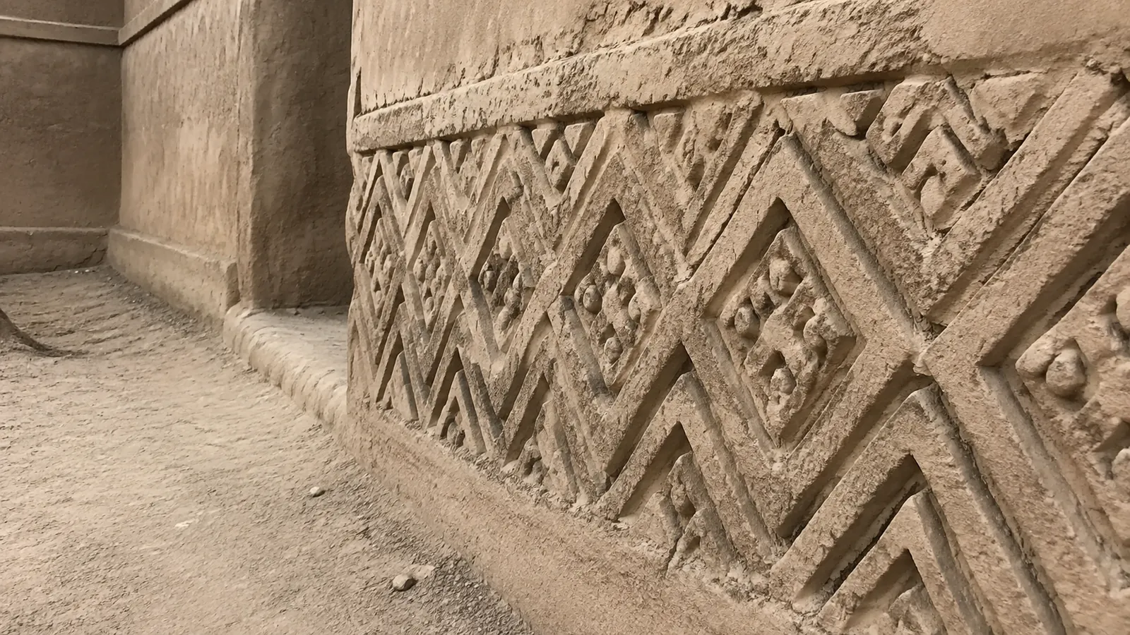 Close view of geometric patterns carved into a weathered earthen wall.