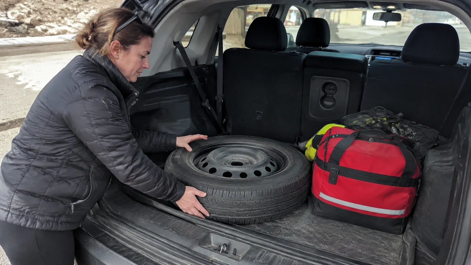 Traveler checks a spare tire beside an emergency bag in a vehicle.