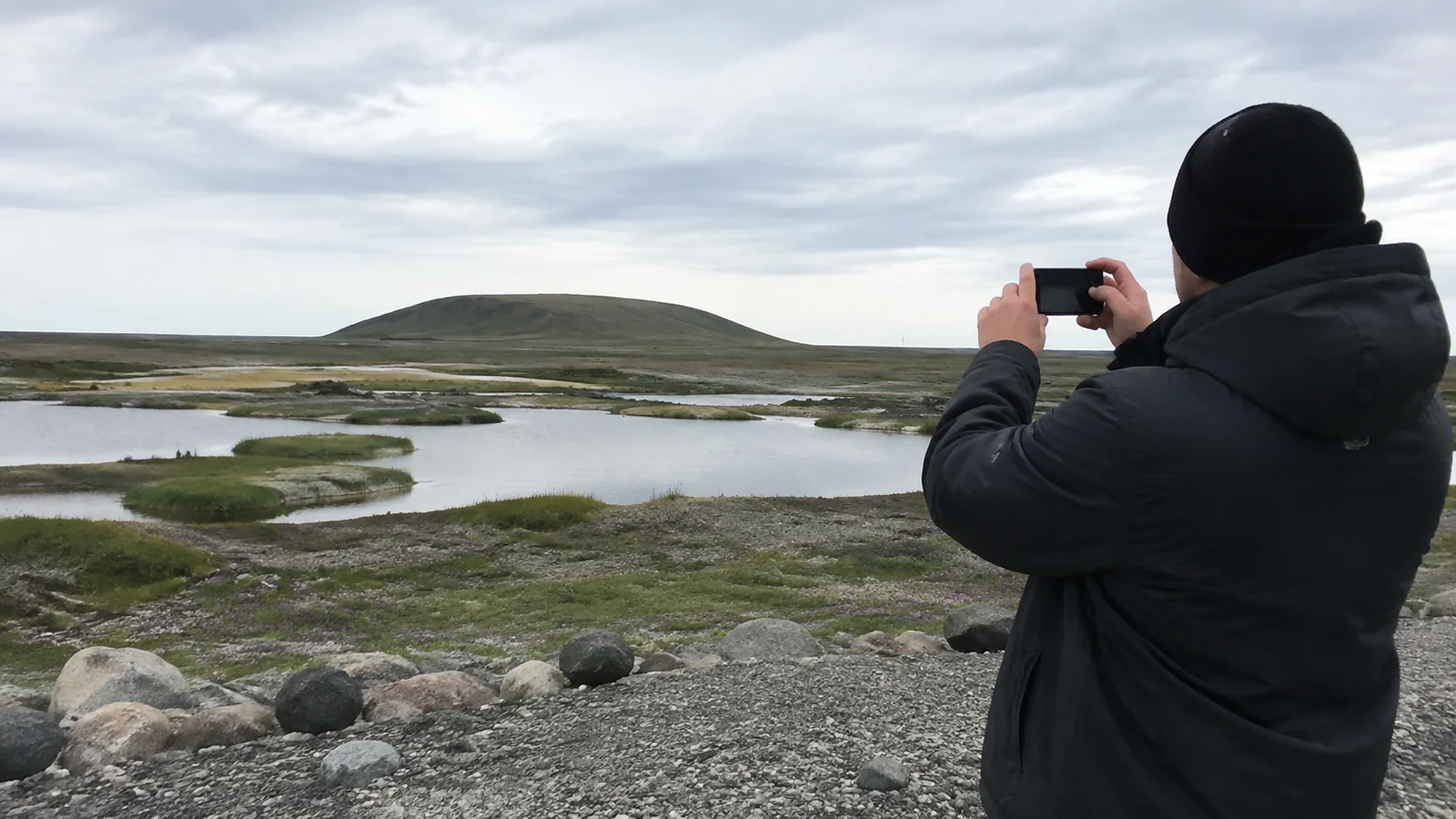 Traveler photographs a rounded hill across a wet tundra landscape.