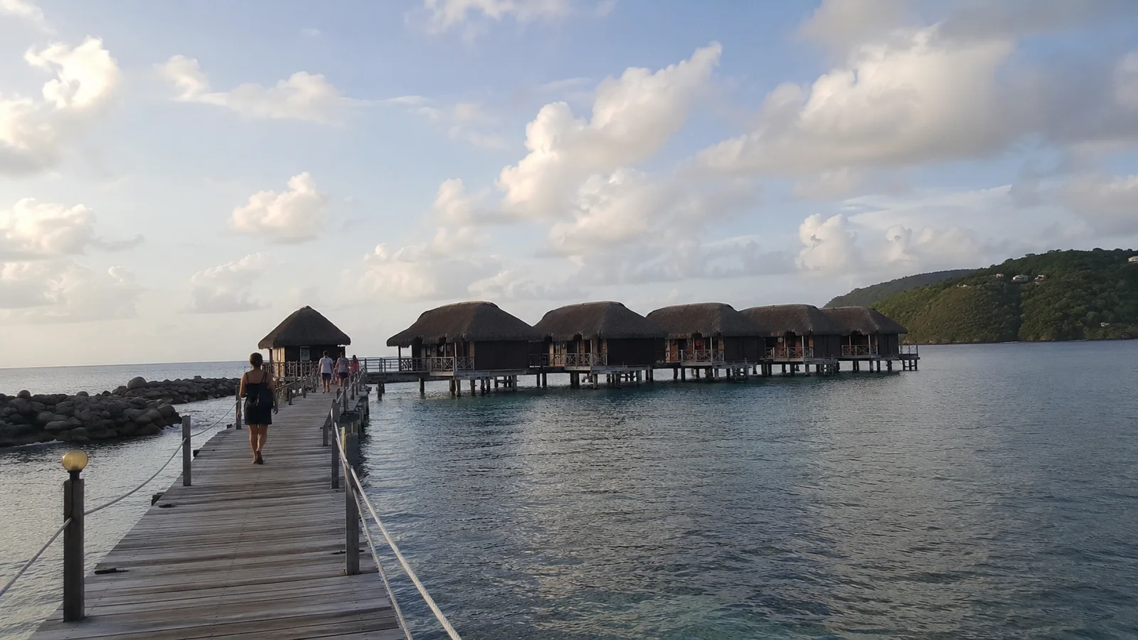 Wooden pier leading to overwater bungalows across calm water at dusk