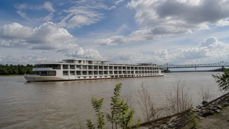 River cruise boat passing a bridge on a broad brown river.