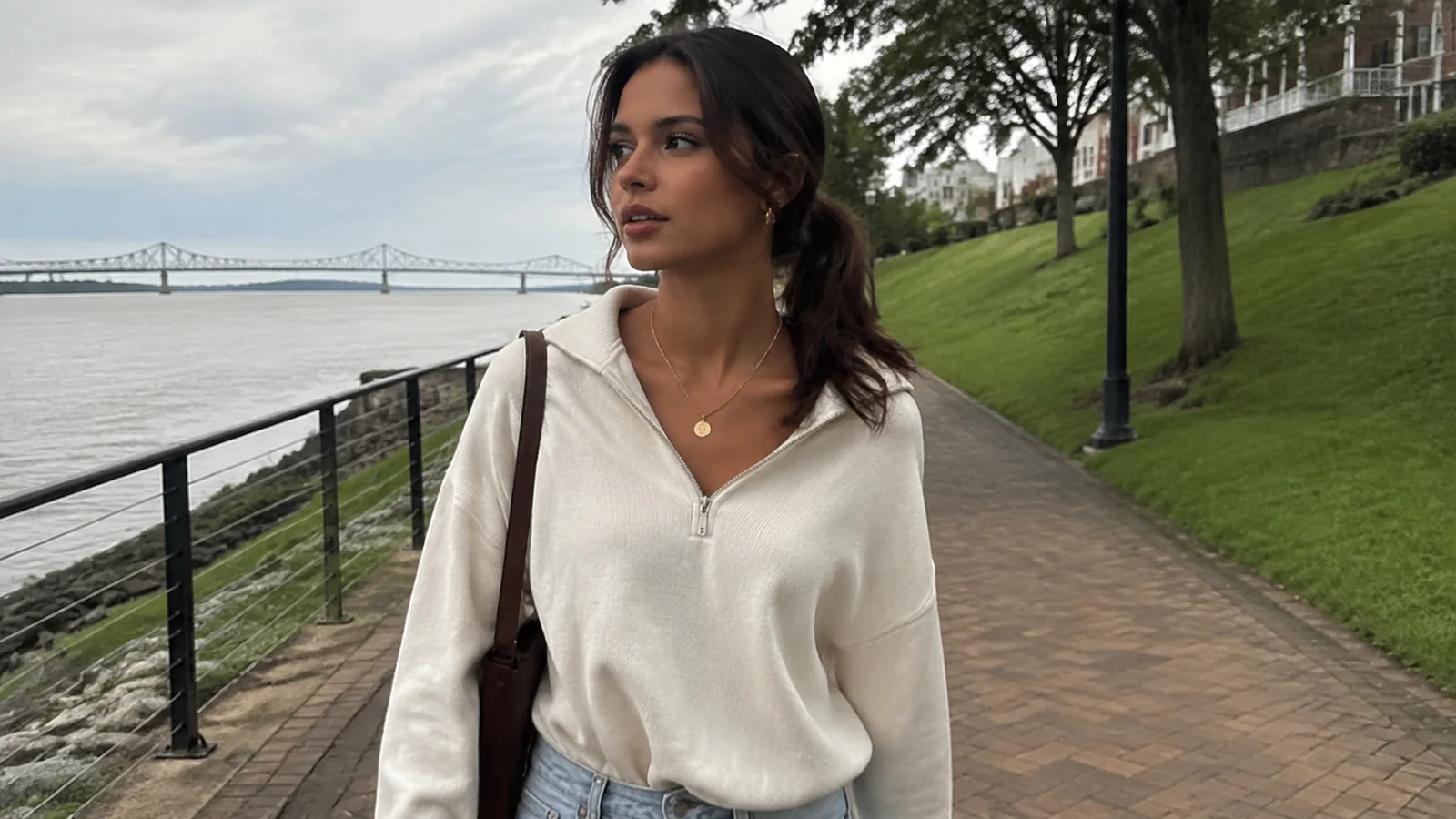 Woman walking along a riverside path below a grassy bank.