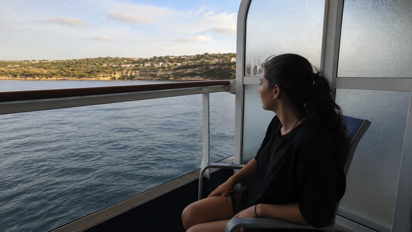 Woman seated on a private ship balcony looking across the water.