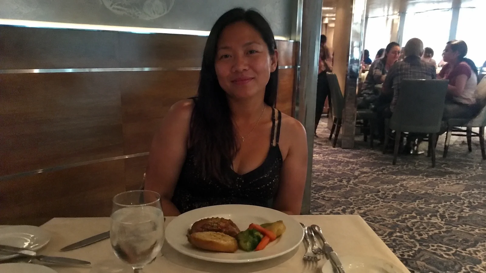 Woman seated behind a plated meal in a wood-paneled restaurant.