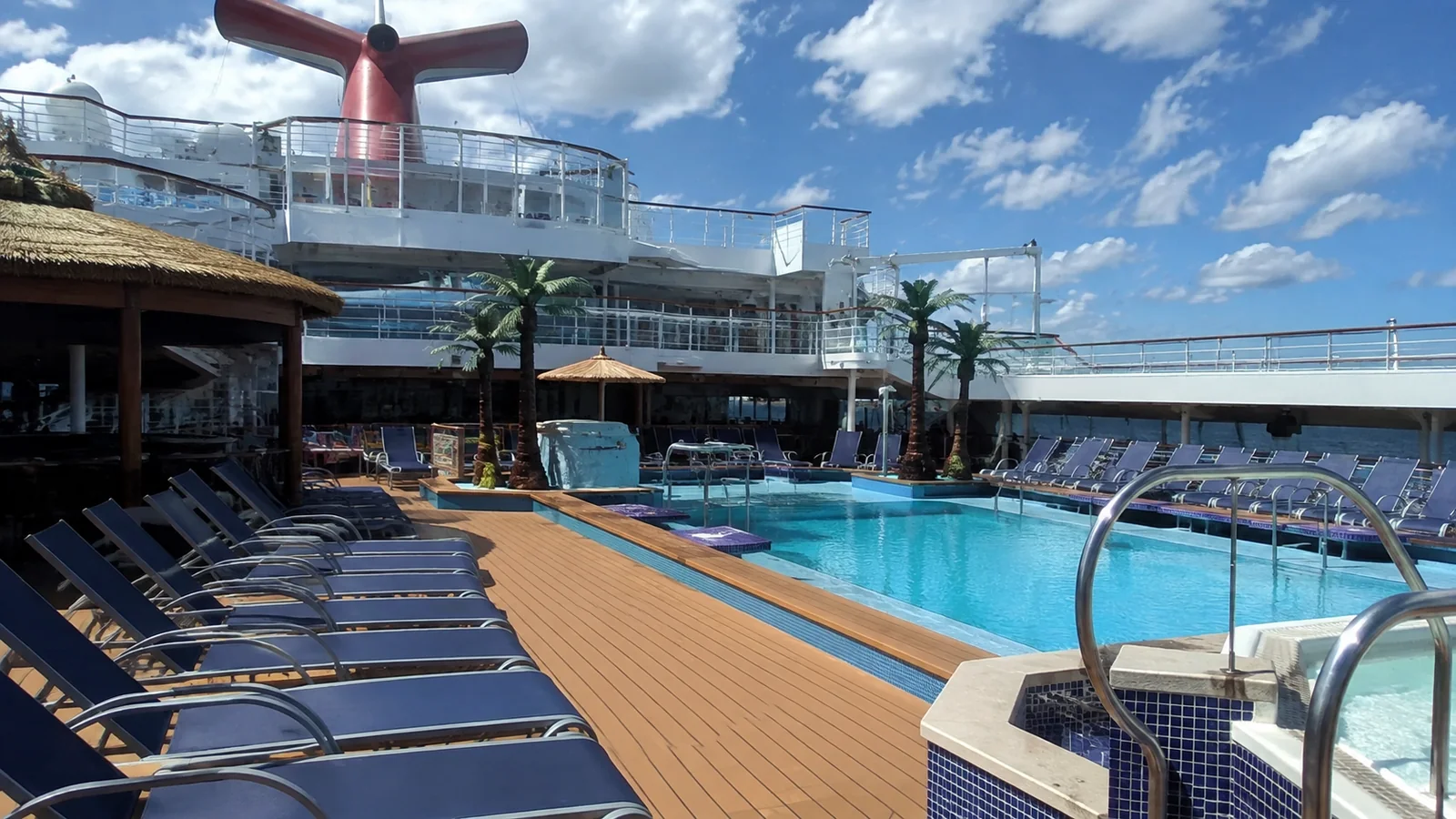Outdoor ship swimming pool surrounded by empty loungers and upper decks.