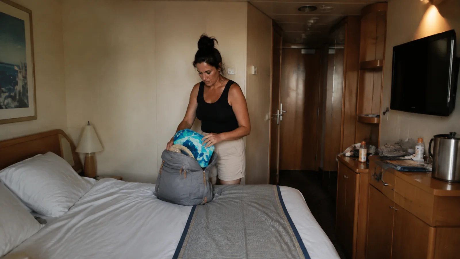Woman packing a gray backpack on the bed in a ship cabin.