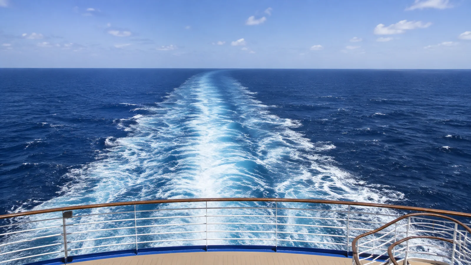 Long foamy wake stretches behind a ship across deep blue ocean.