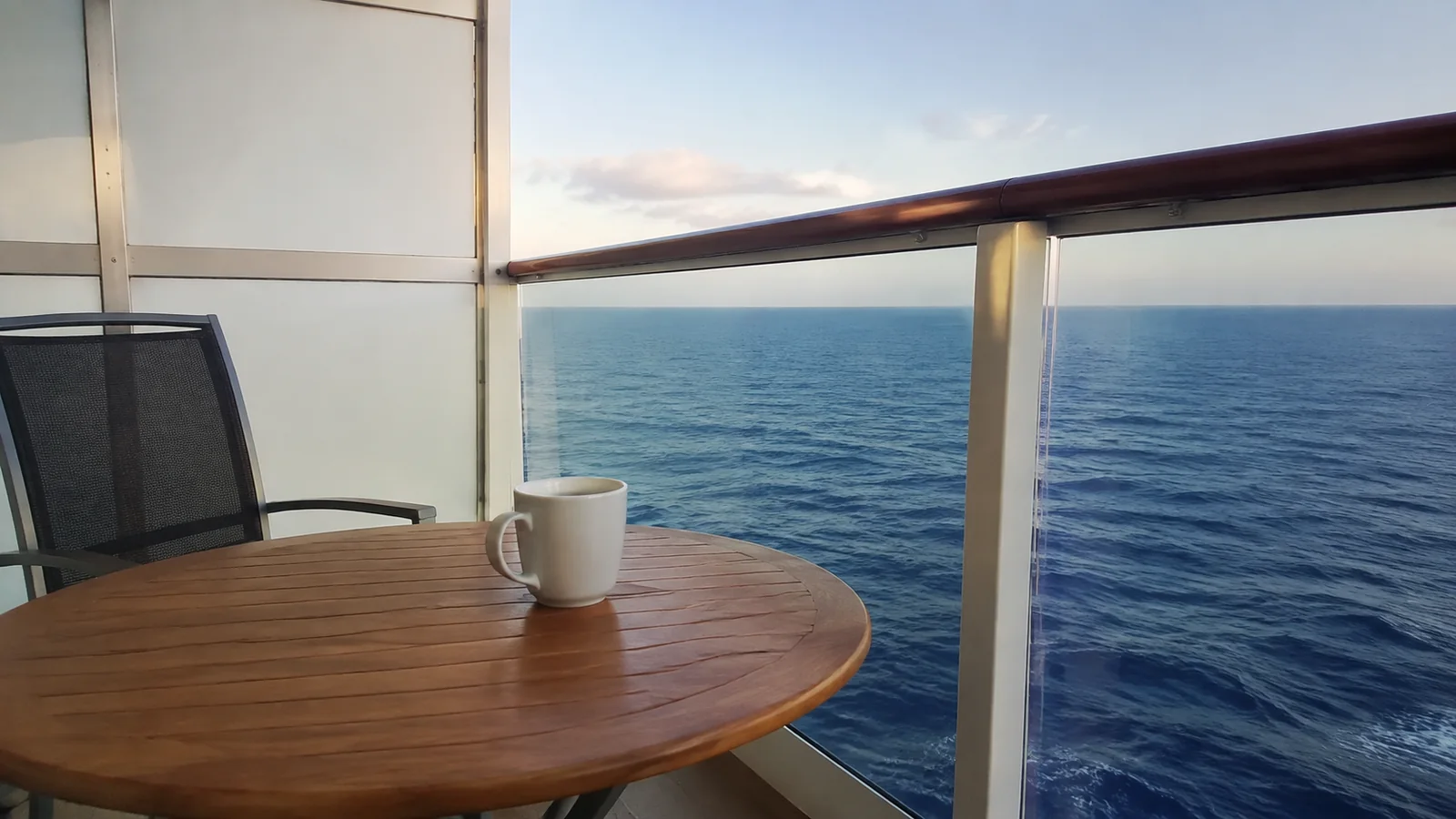White mug on a round wooden balcony table overlooking the sea.