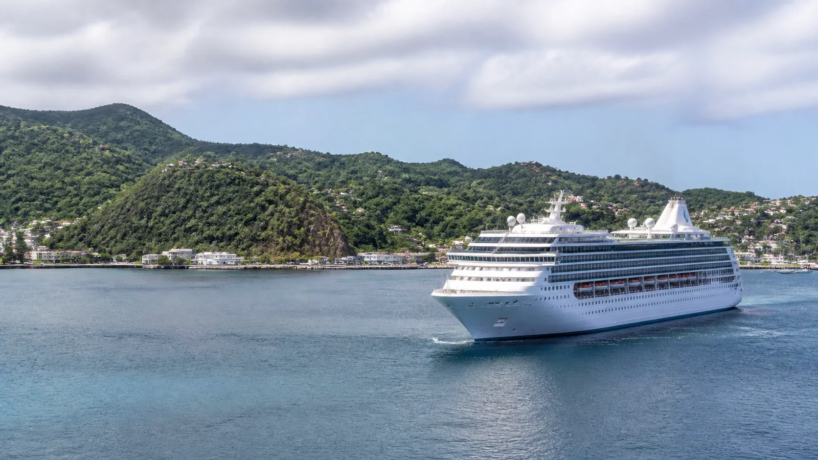 White cruise ship floats near a green hilly shoreline.