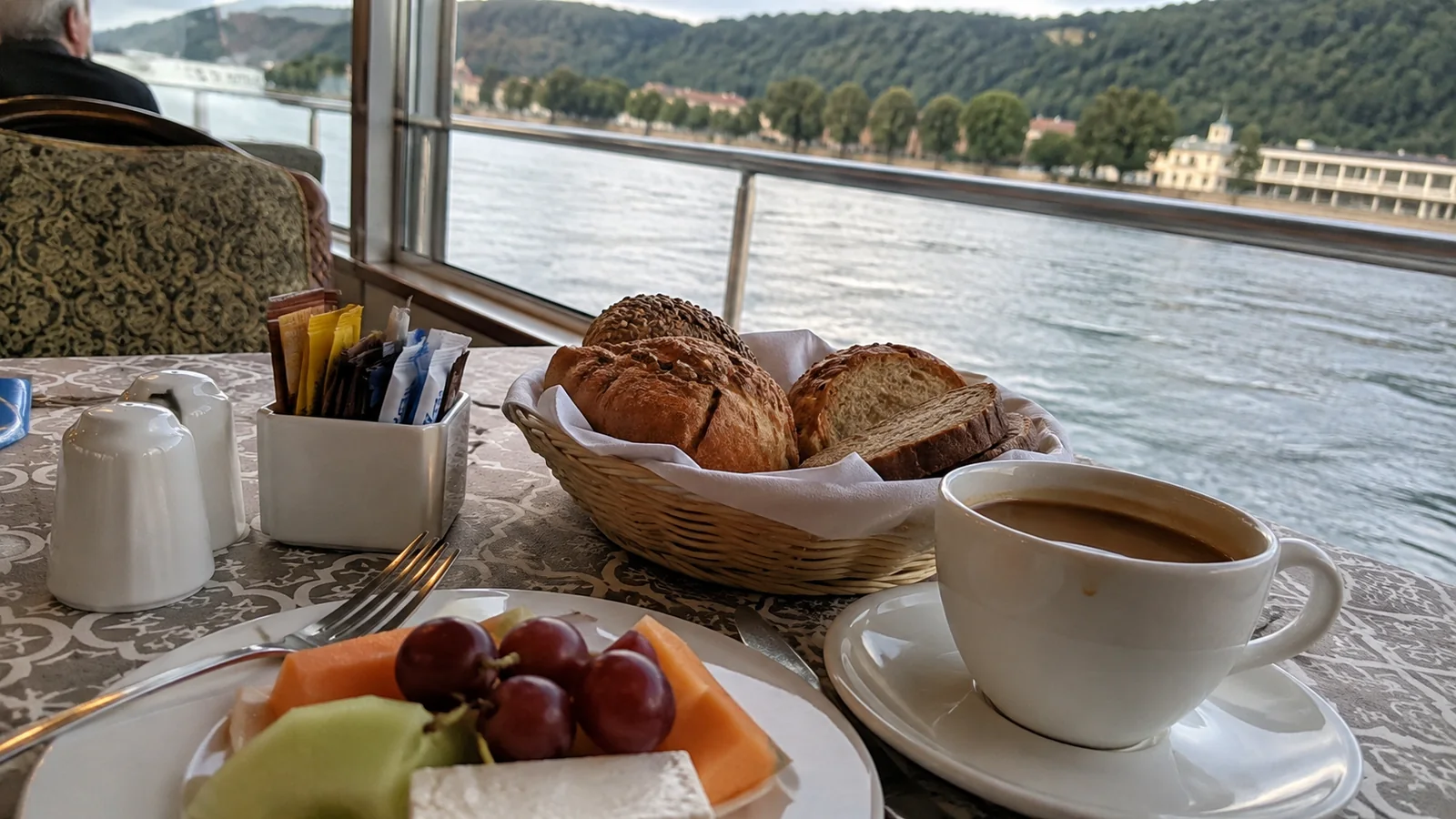 Breakfast with coffee, fruit and pastries beside a river-view window.