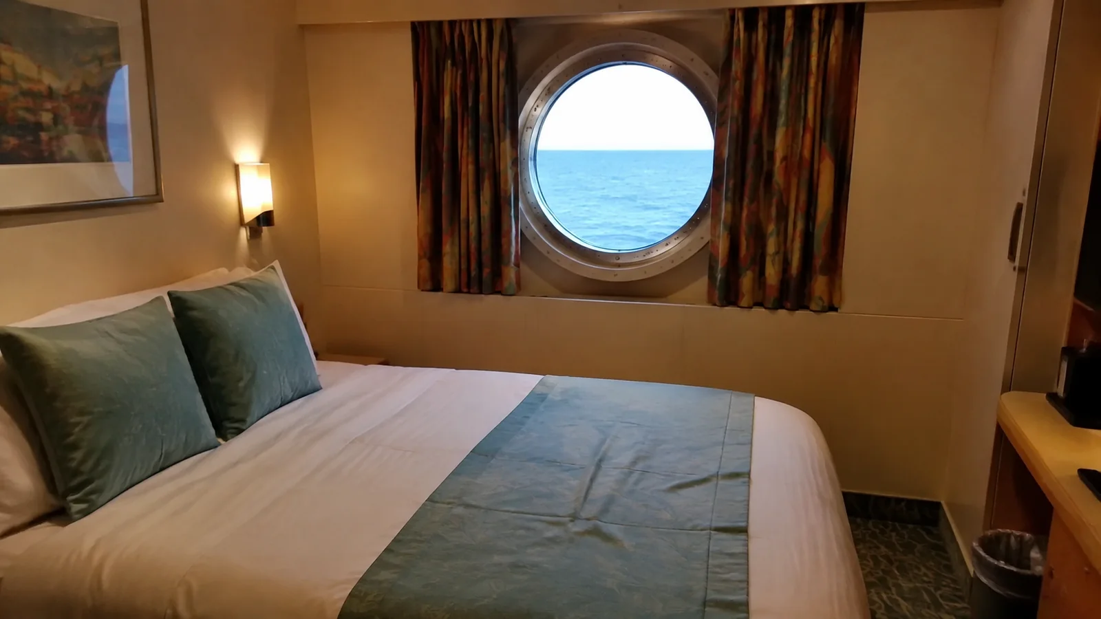 Compact stateroom bed sits beneath a round ocean porthole.