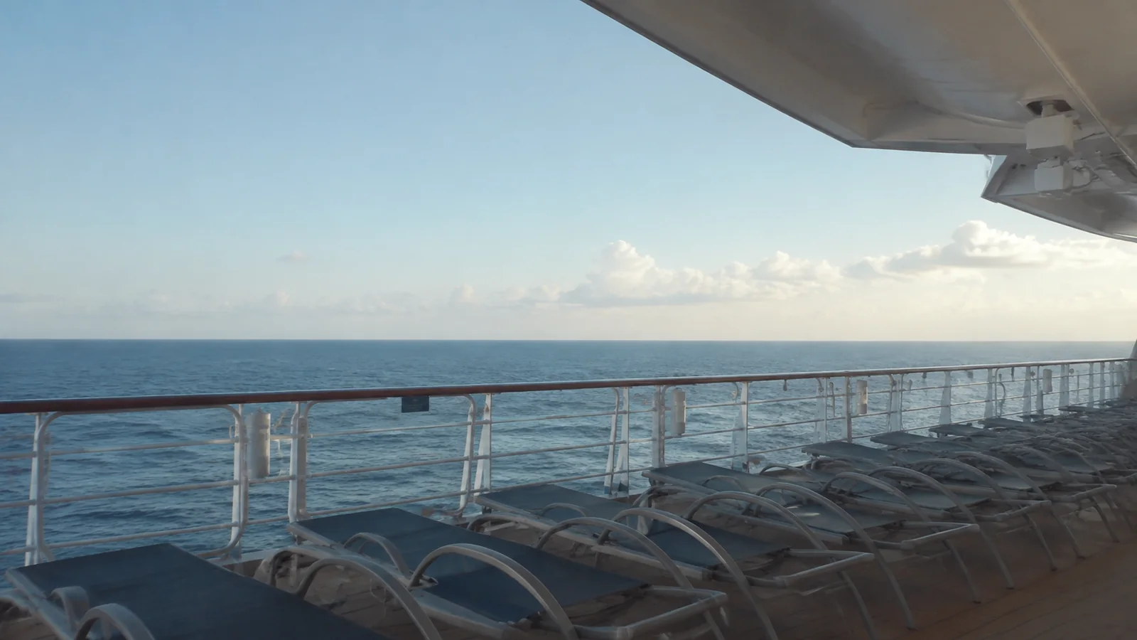 Empty deck loungers face the sea beneath a ship overhang.