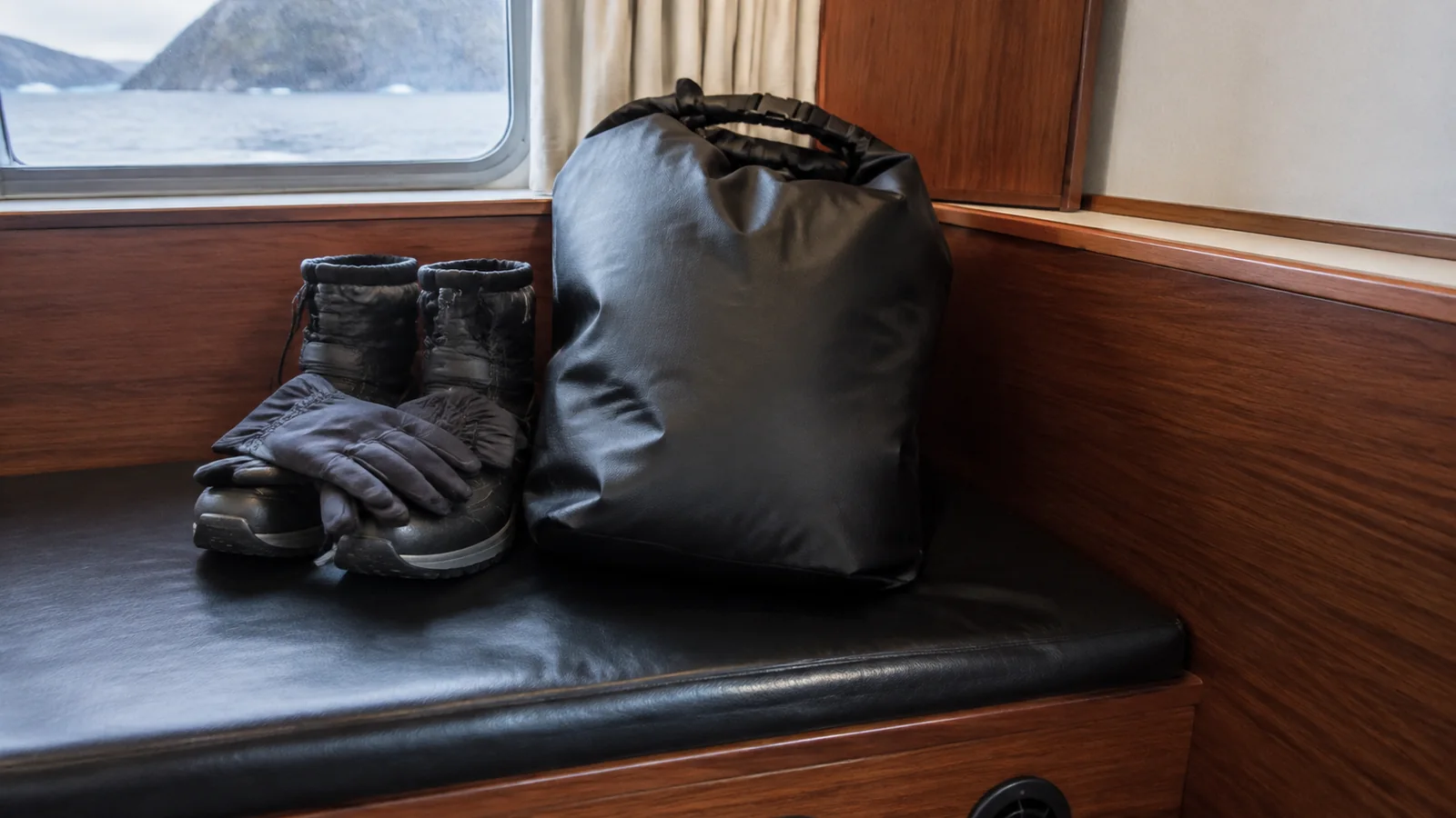 Winter boots, gloves, and a waterproof bag on a ship bench.