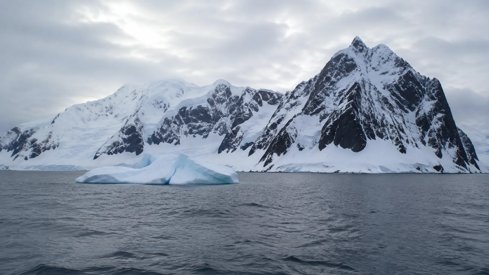 Snow-covered mountain peaks rise above dark water and floating ice.