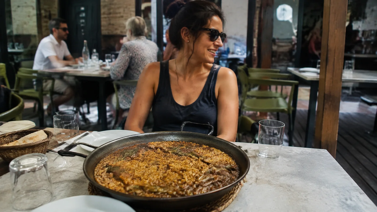 Woman seated at an outdoor table with a large pan of rice.