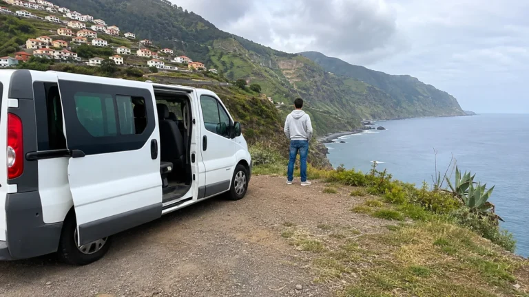 White passenger van parked at a coastal overlook while a man looks out over the sea