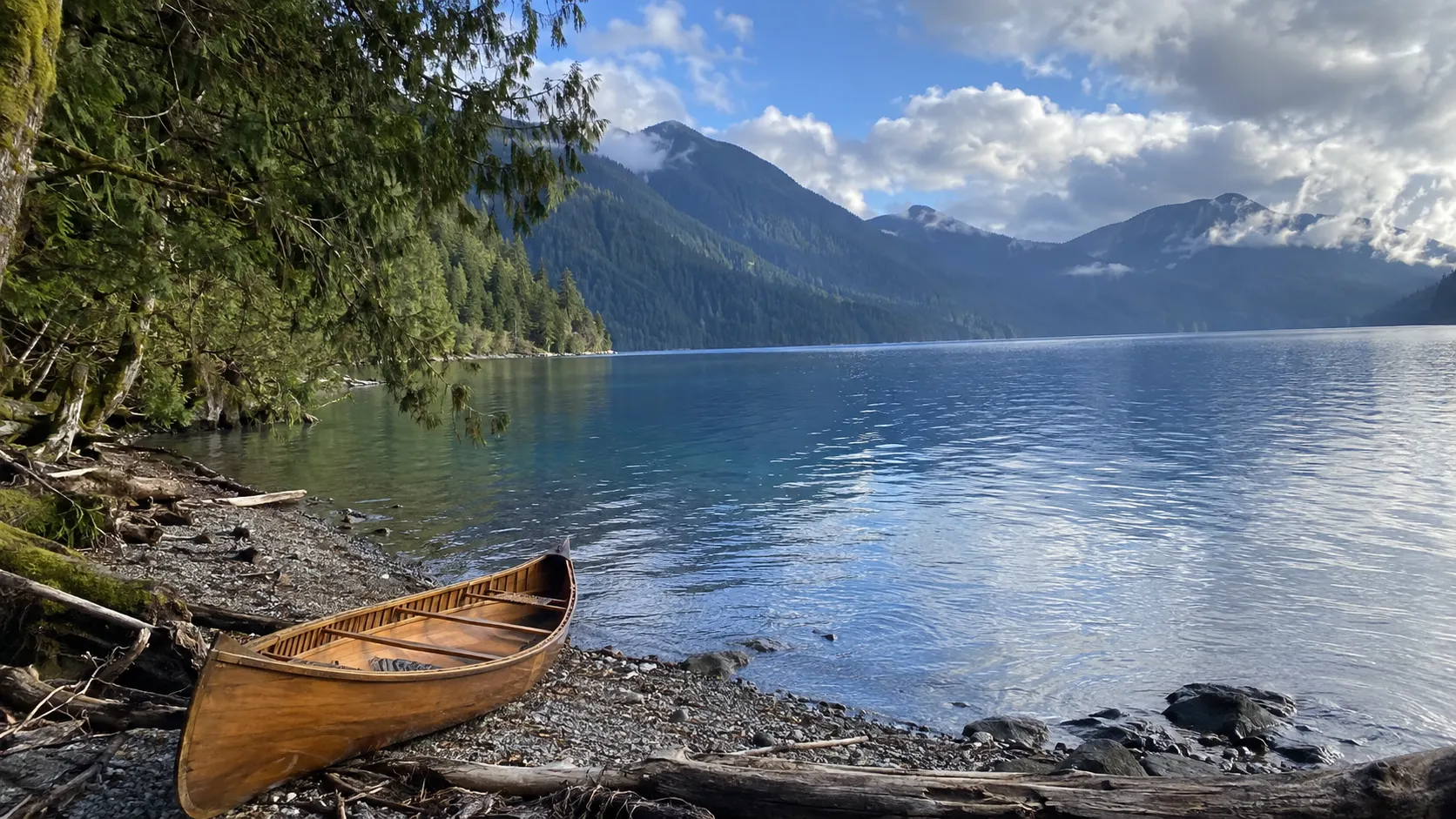 Wooden canoe pulled onto the forested shore of deep-blue Lake Crescent in Olympic National Park.