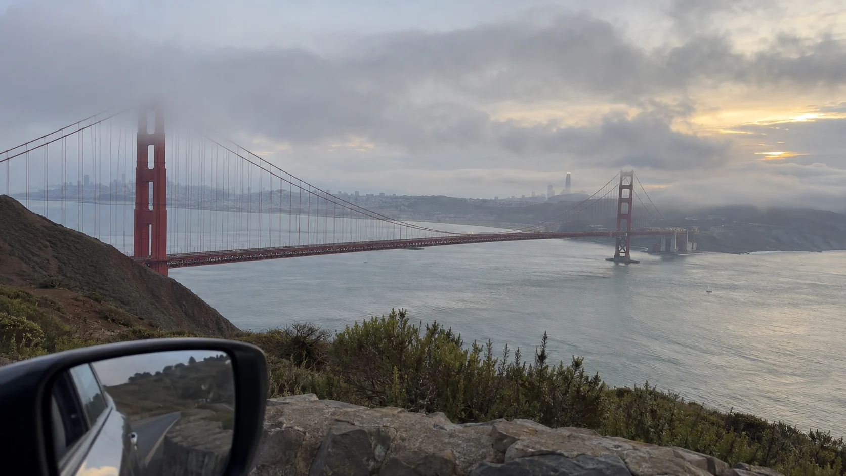 Golden Gate Bridge emerging through fog above a road-trip car mirror at the Marin Headlands.