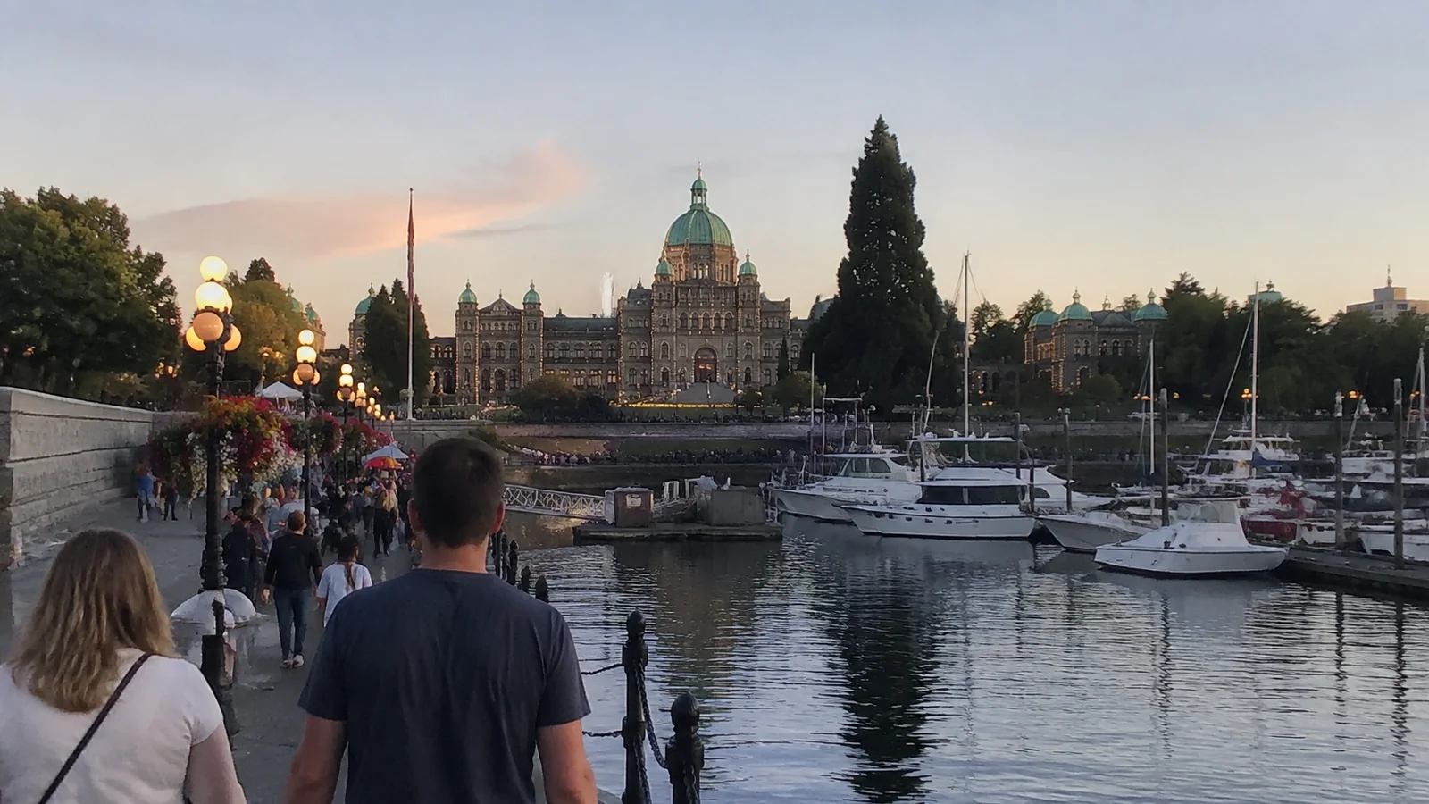 Visitors walking beside Victoria's Inner Harbour with the domed Parliament Buildings beyond.