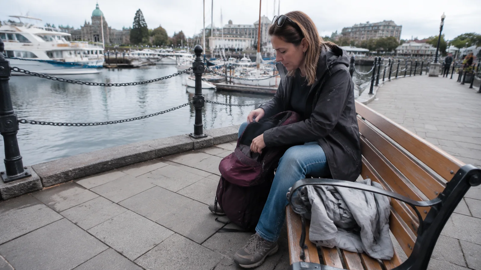 Traveler searching a backpack on a bench beside the harbor.