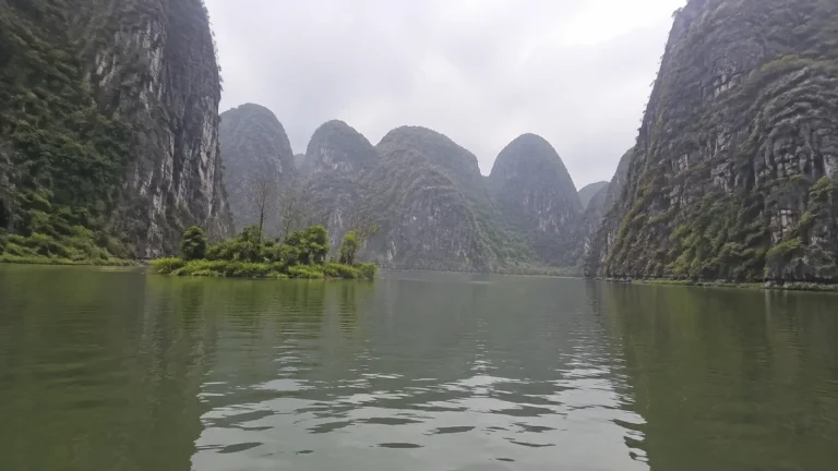 Steep green limestone cliffs rise above calm gray water.