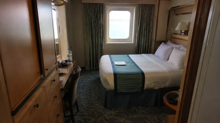 Cruise cabin with a double bed, wooden cabinets, and ocean-view window