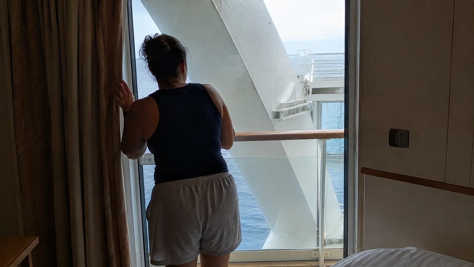 Woman standing in a balcony doorway facing a large diagonal ship support