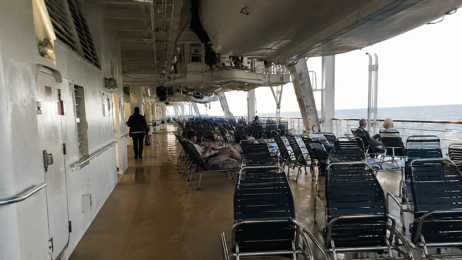 Rows of lounge chairs along a covered cruise ship promenade